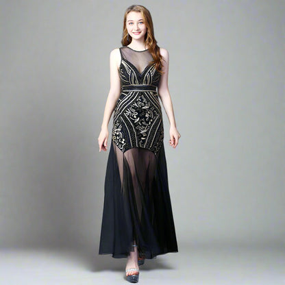 A model wearing an elegant, sleeveless, mini dress with a geometric pattern in black, white, and silver colors, featuring a high neck and a mid-calf length.